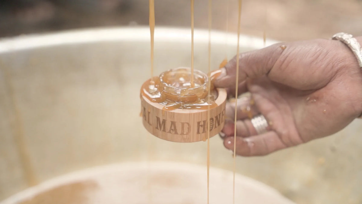 A glass jar being filled by hand with fresh raw honey